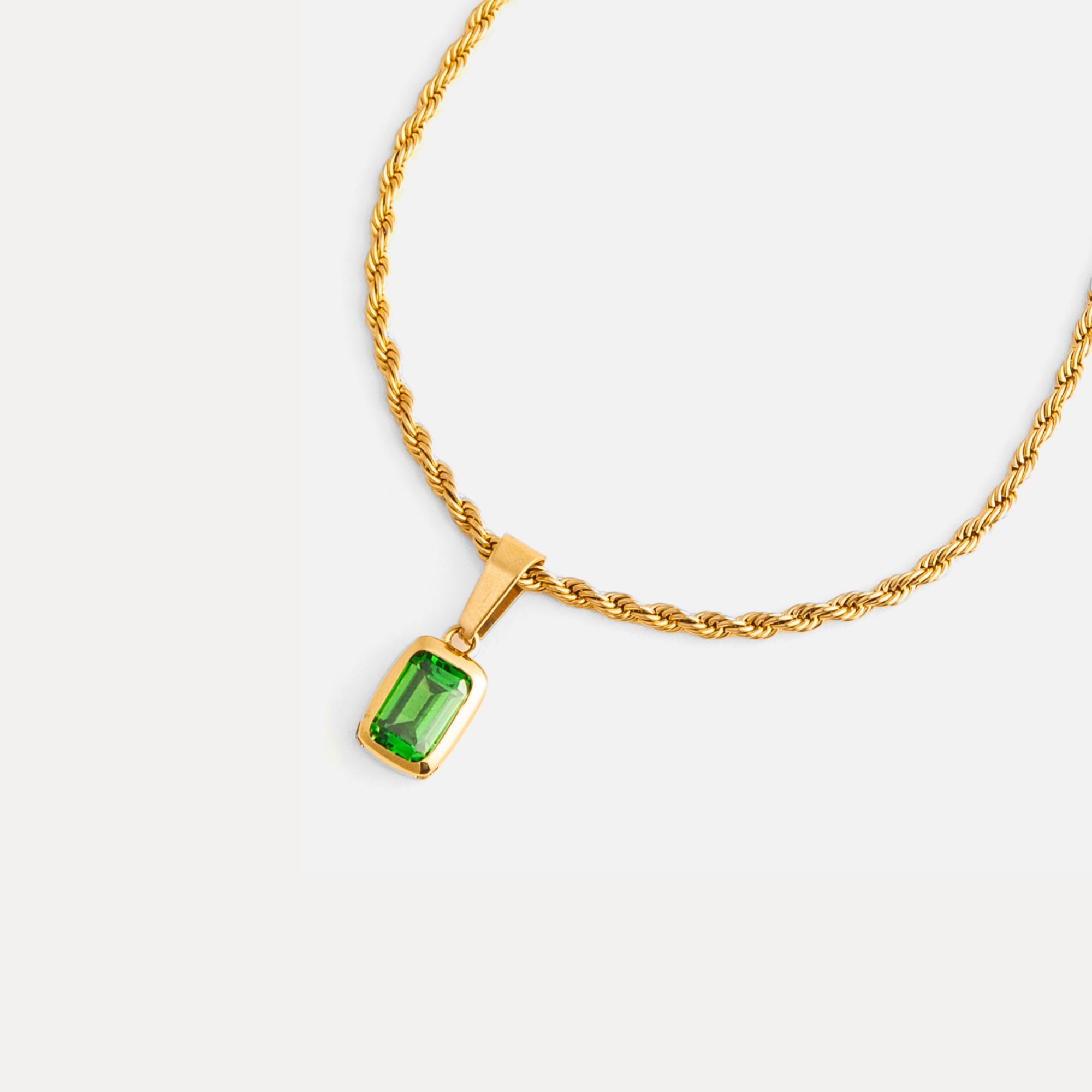Gold necklace with a green gemstone pendant on a white background