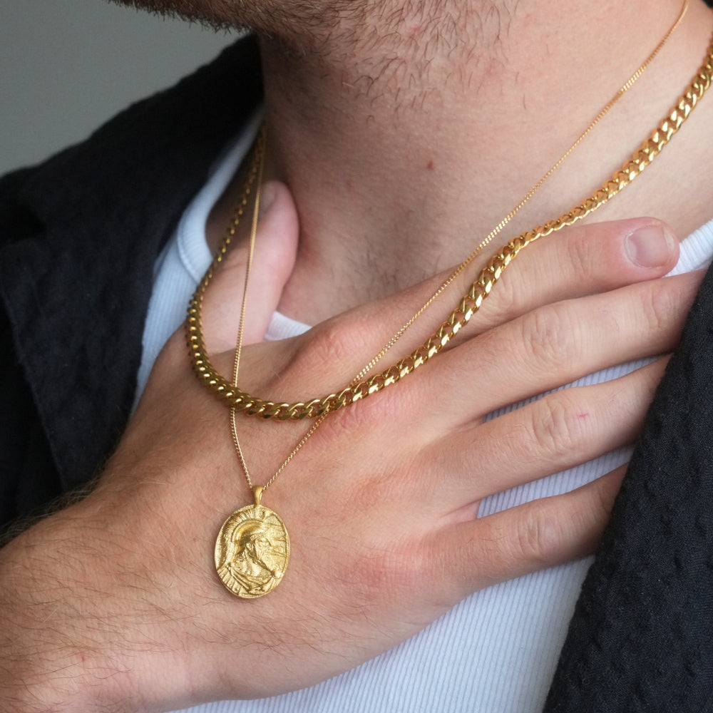 Close-up of a person wearing a gold chain necklace with a pendant.