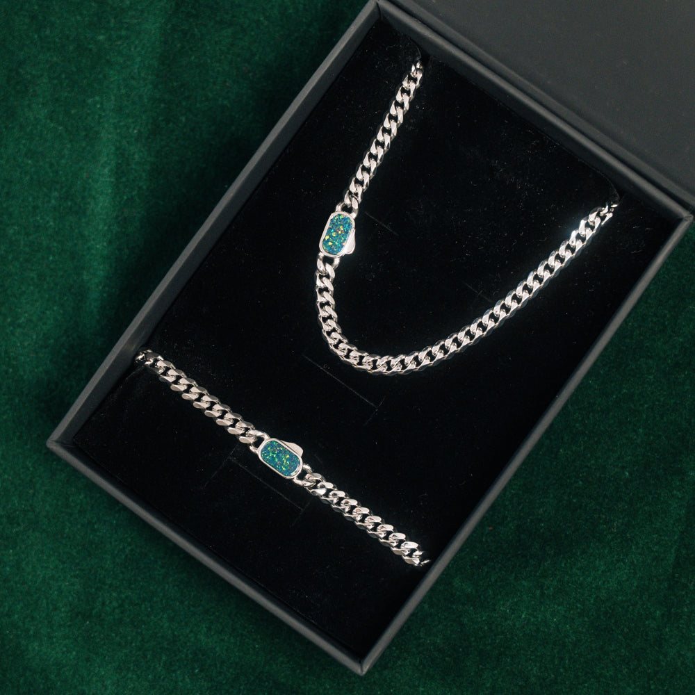 Silver chain bracelet with green stones in a black jewelry box on a green background