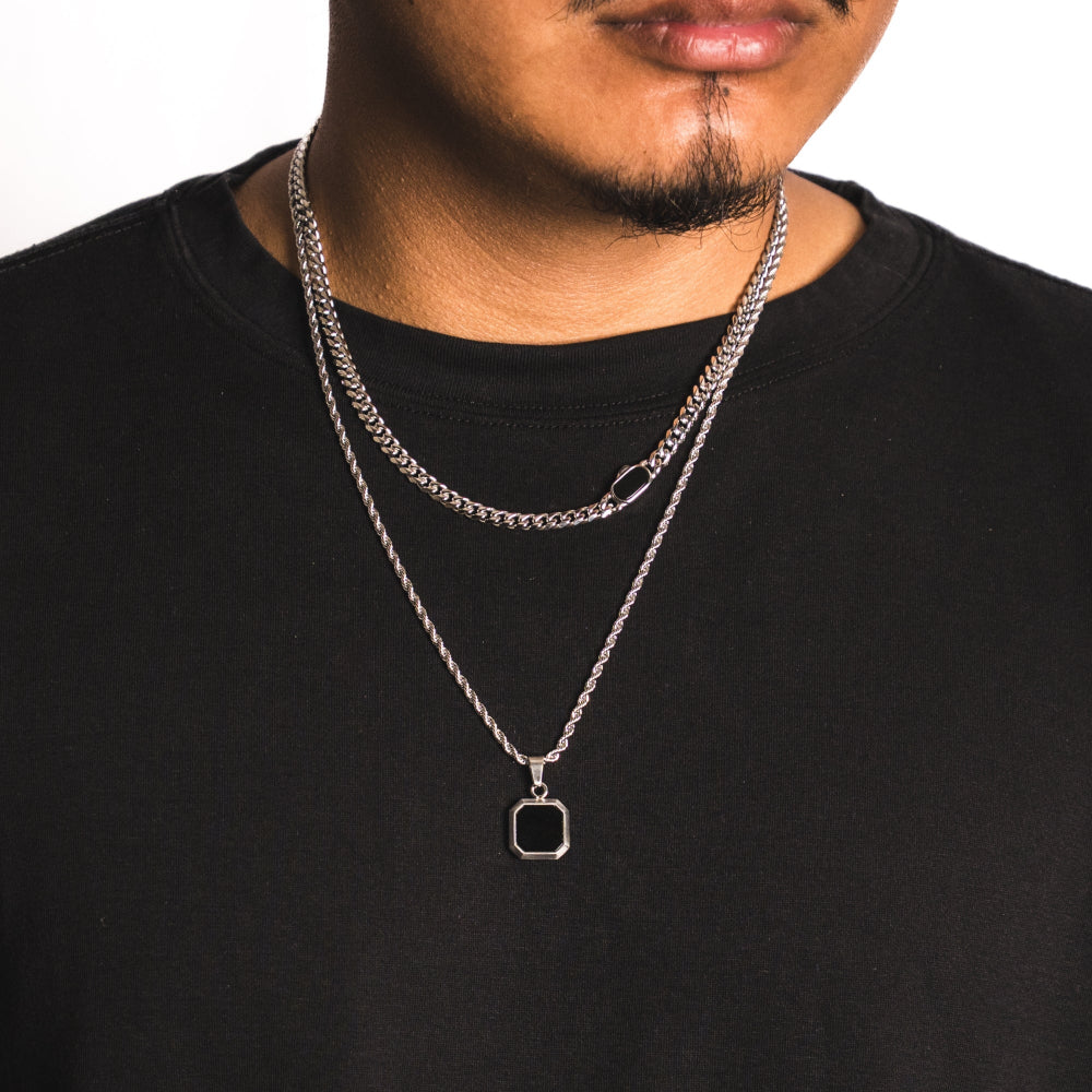 Person wearing a black shirt with two silver necklaces, one with a square pendant.