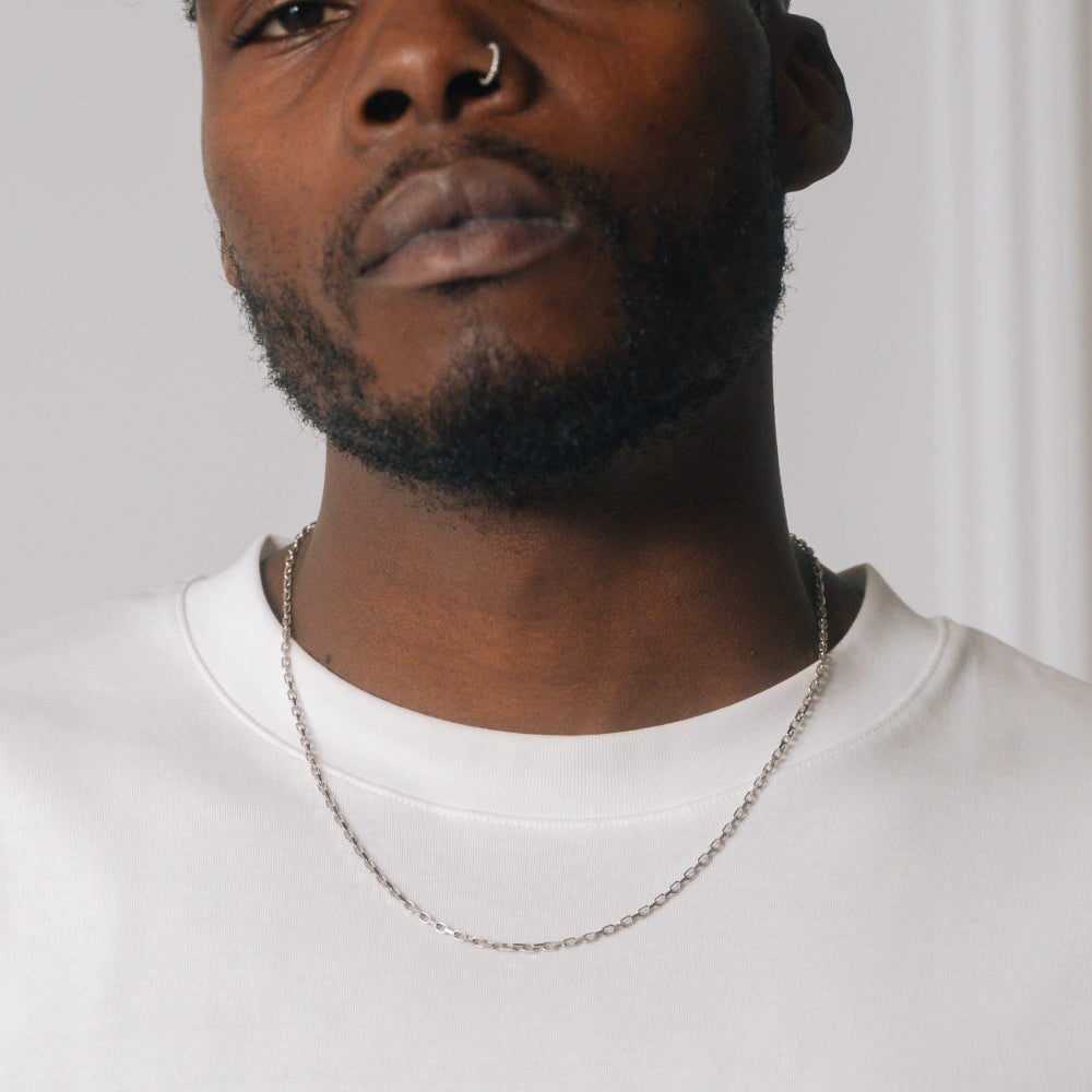 Man wearing a silver chain necklace against a plain background