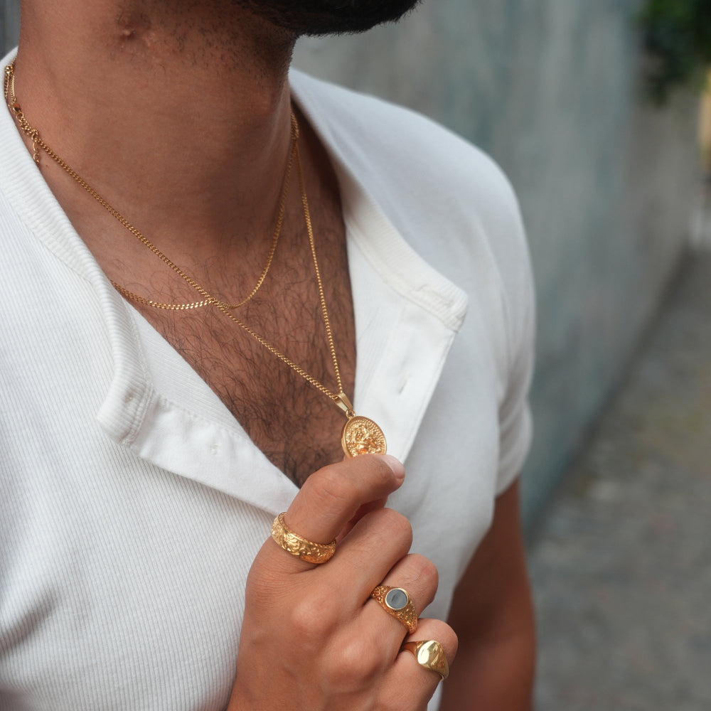 Person wearing gold jewelry including a necklace, ring, and bracelet.