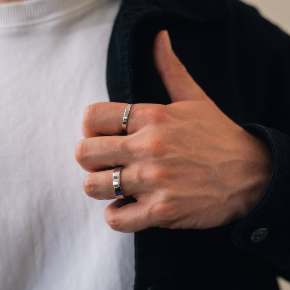 Close-up of a person's hand wearing two silver rings on a neutral background