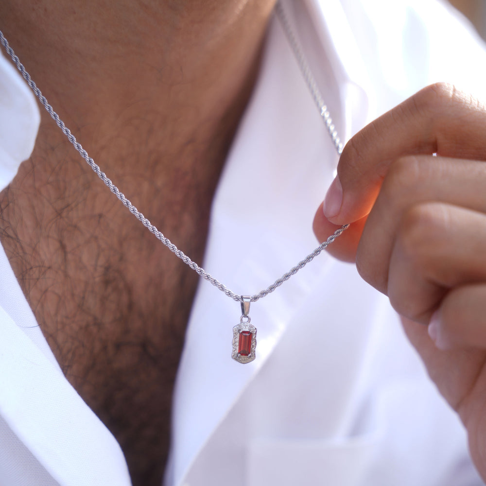 Person holding a silver necklace with a red pendant
