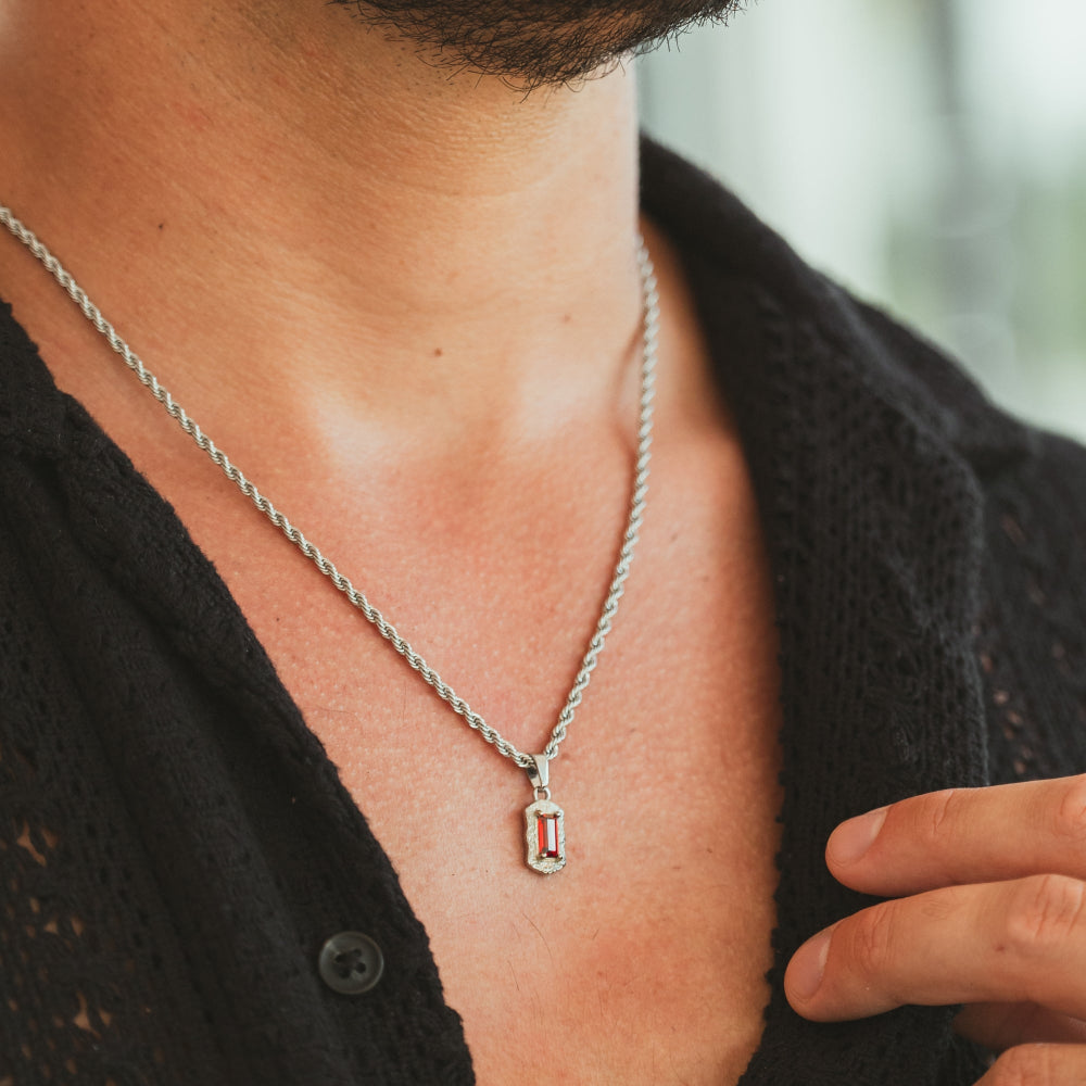 Person wearing a silver necklace with a red stone pendant