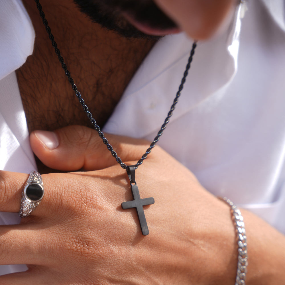 Person wearing a black cross necklace with a white shirt background