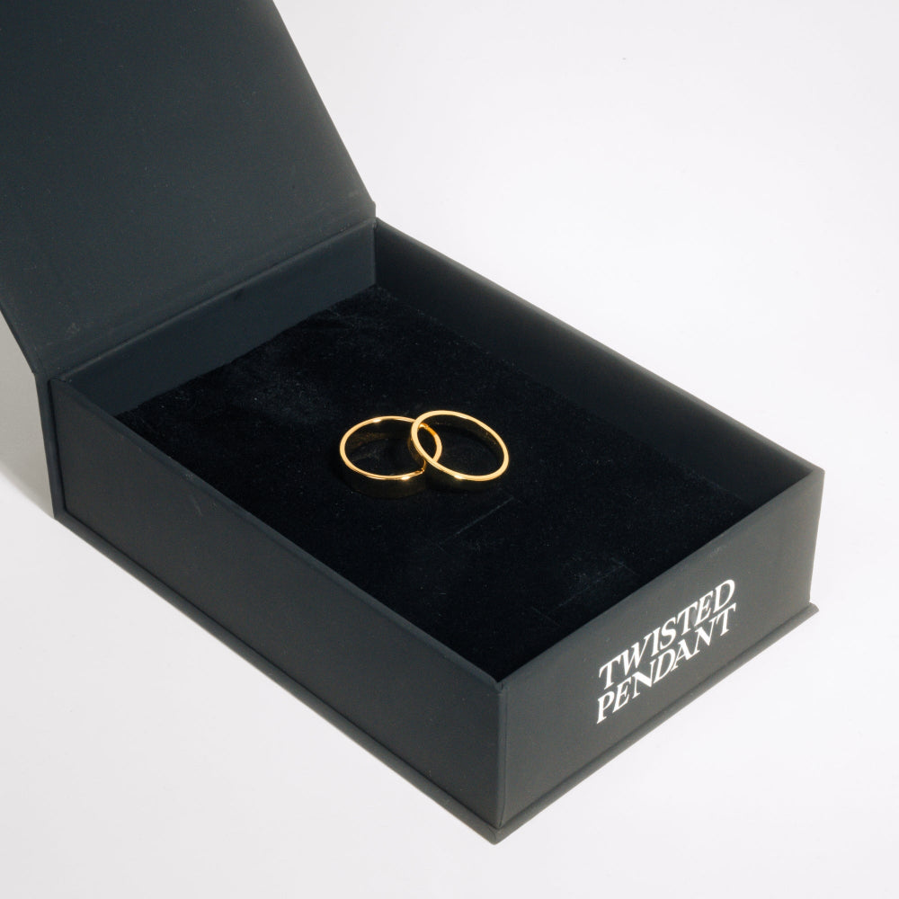 Gold rings in a black jewelry box labeled 'Twisted Pendant' on a white background