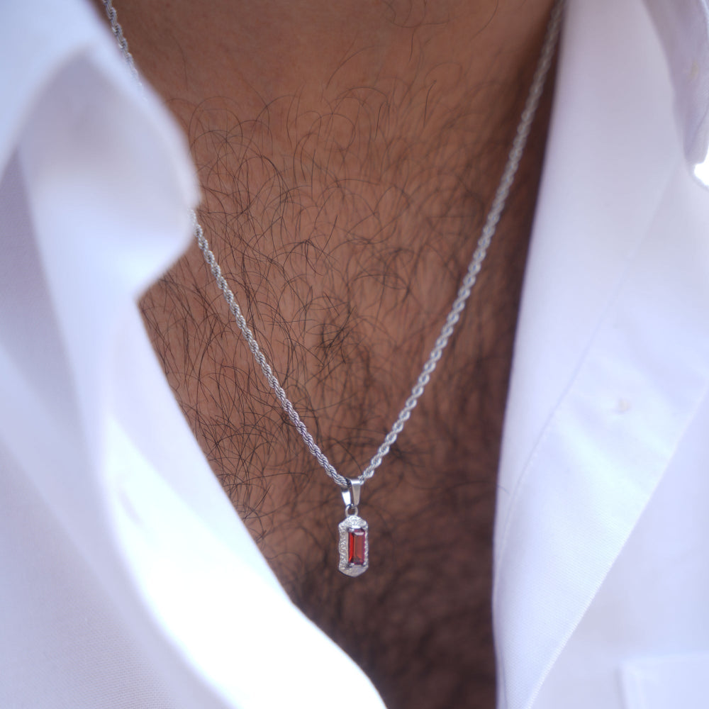 Silver necklace with a red pendant worn by a person in a white shirt.