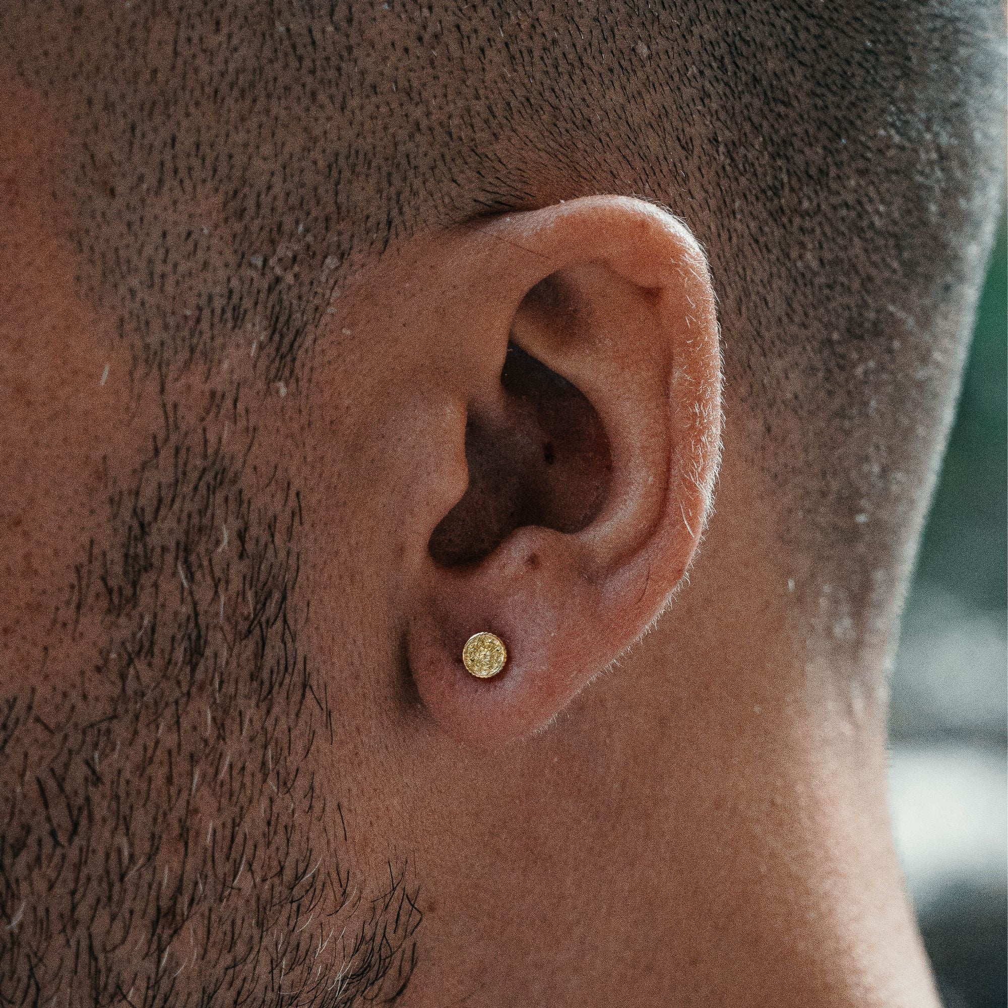 A close-up of a man's ear wearing a small round gold stud earring.