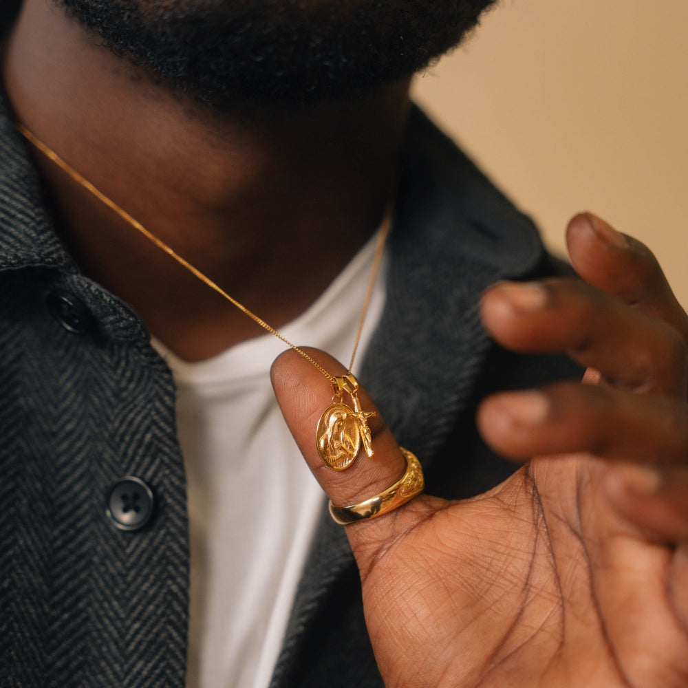 Person wearing a gold necklace and ring, with a blurred background
