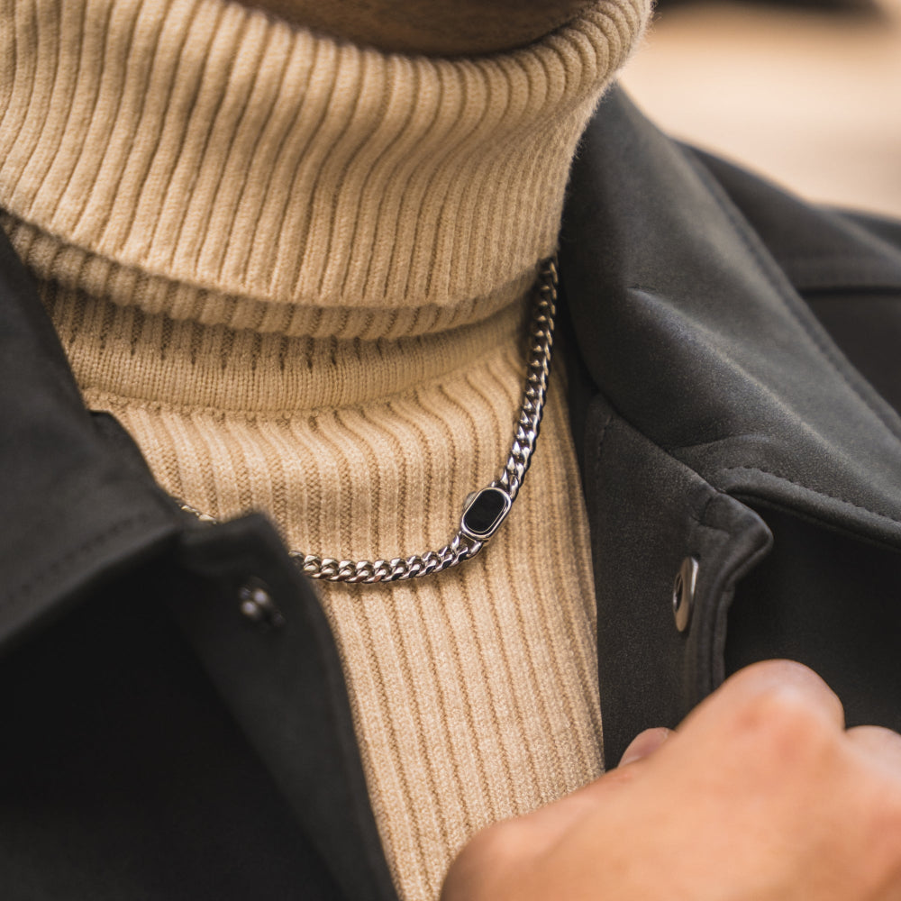 Person wearing a beige turtleneck sweater and dark coat with a chain necklace.