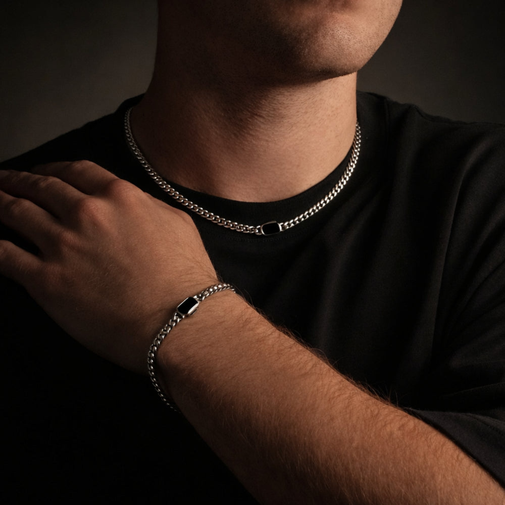 Person wearing a silver chain necklace and bracelet on a dark background