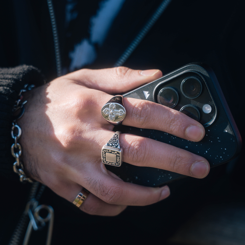 Hand holding a smartphone with multiple rings on fingers against a dark background