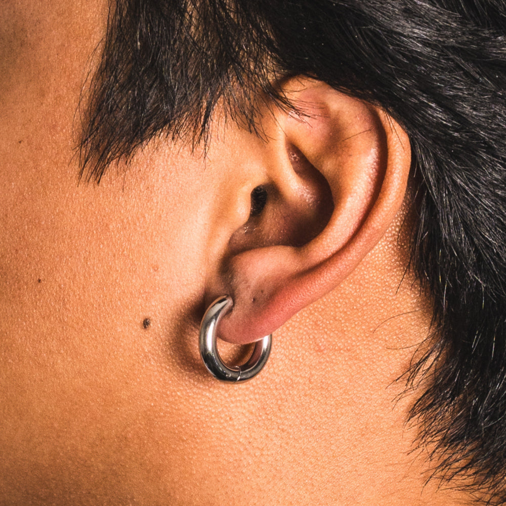Close-up of an ear with a silver hoop earring on a person with dark hair.