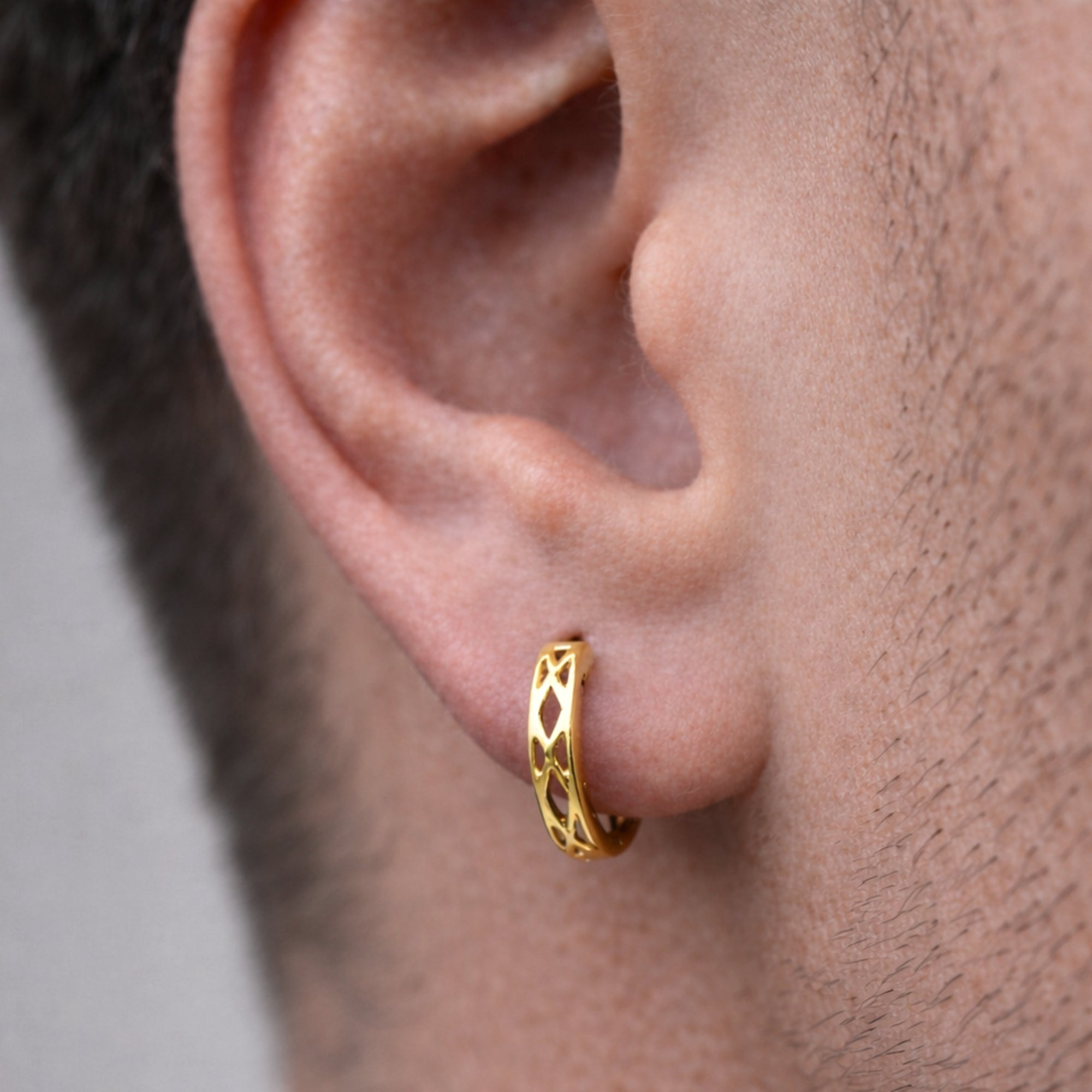Gold hoop earring worn by a person with a neutral background