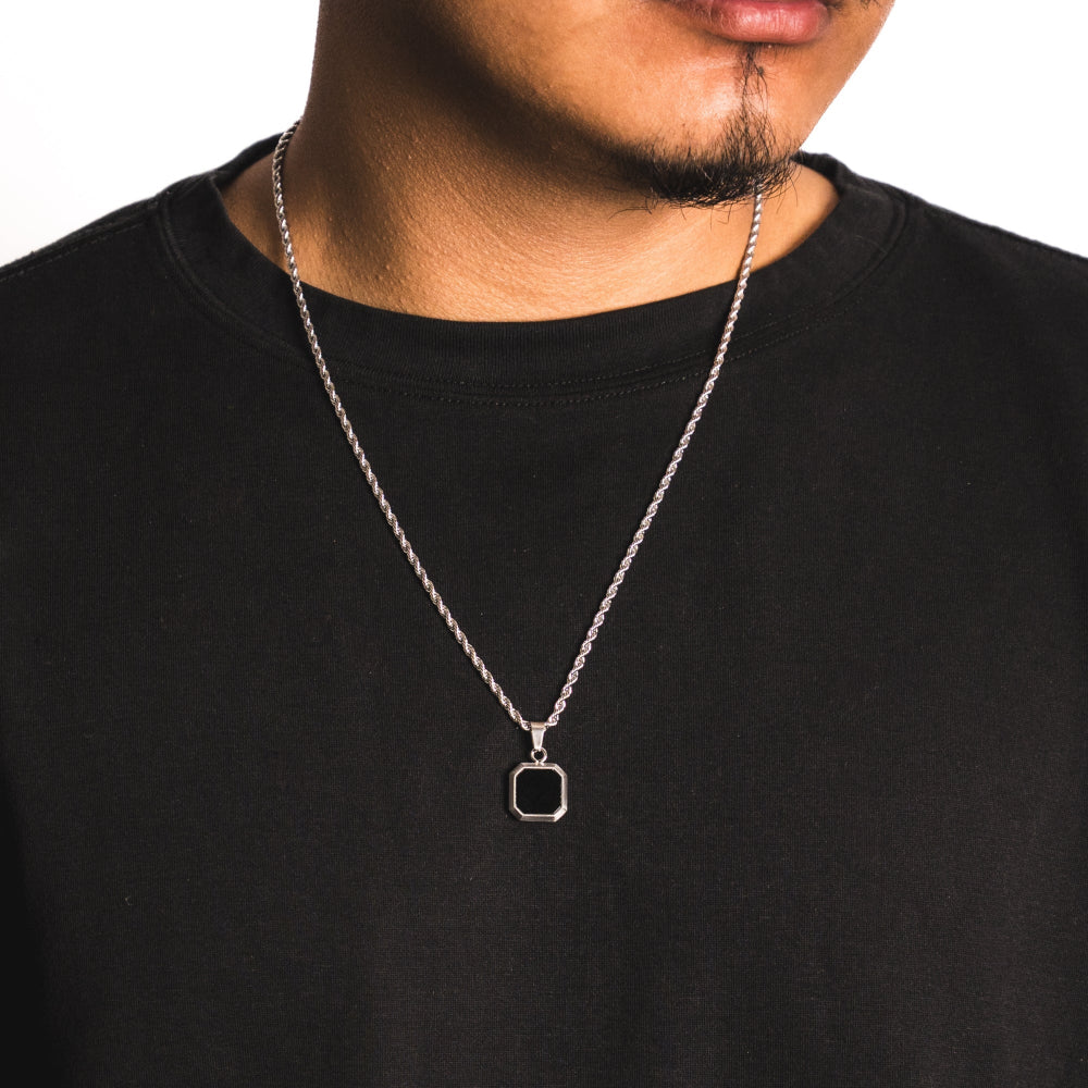 Person wearing a black shirt with a silver necklace featuring a square pendant.