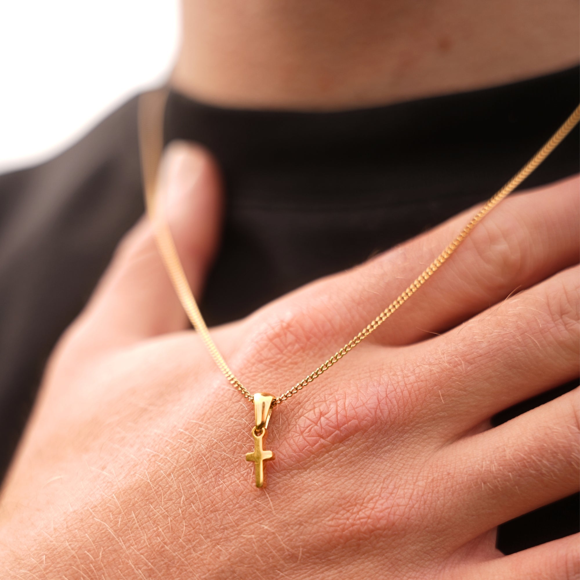 Gold necklace with a cross pendant held by a hand against a neutral background