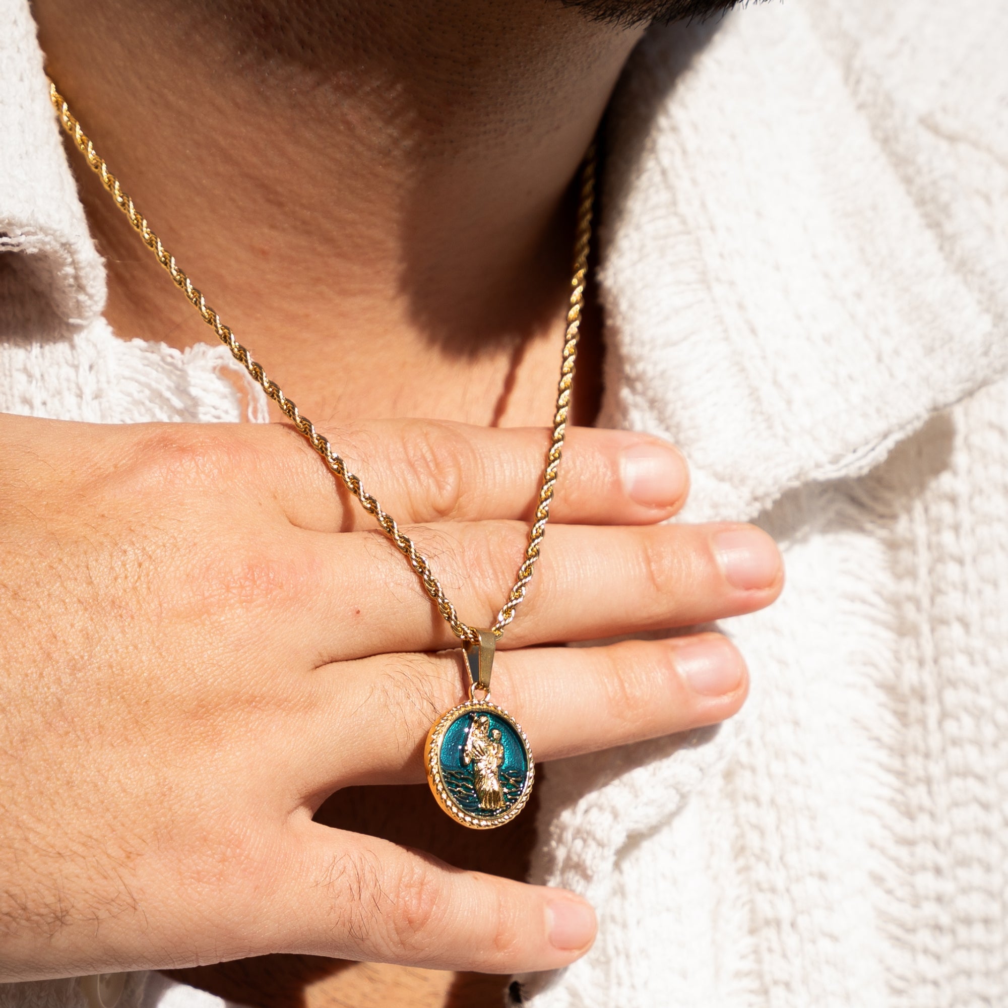 Close-up of a hand holding a gold necklace with a pendant, wearing a white sweater.