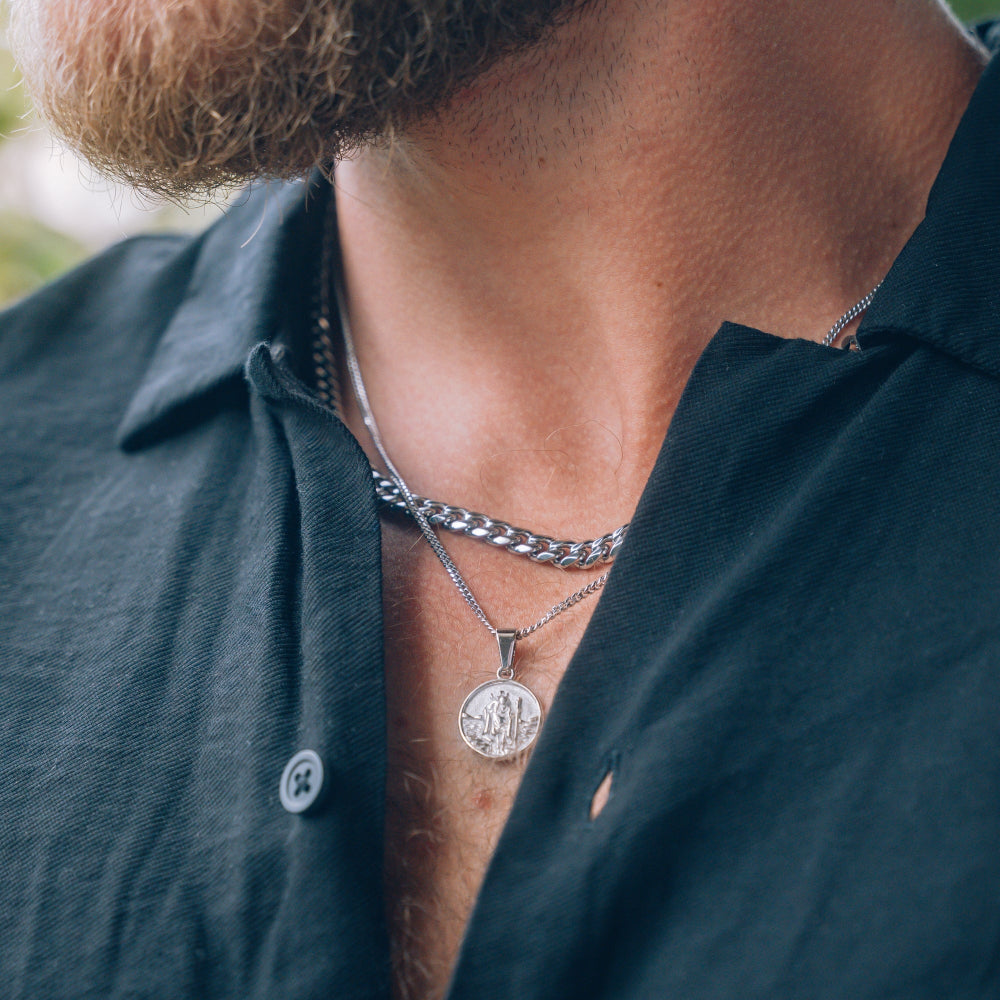 Close-up of a person wearing two silver necklaces with circular pendants on a blurred background.