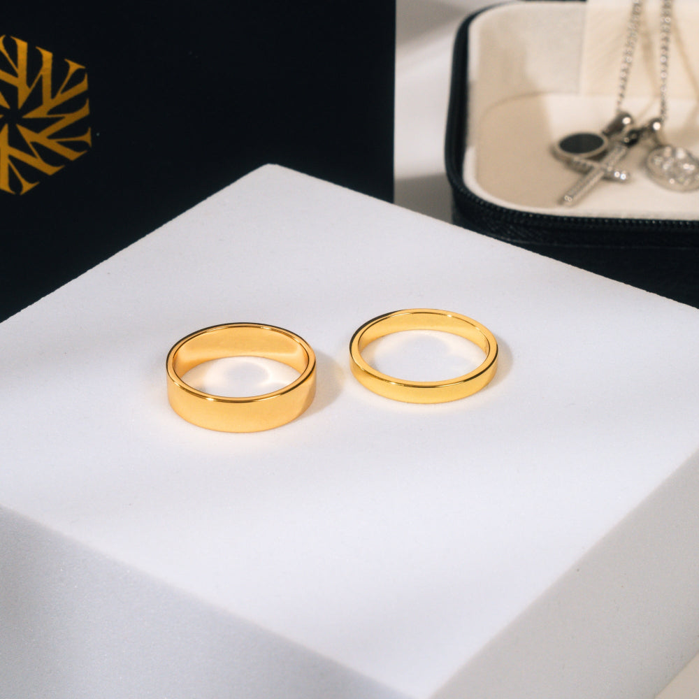 Two gold rings on a white surface with a black and gold box in the background.