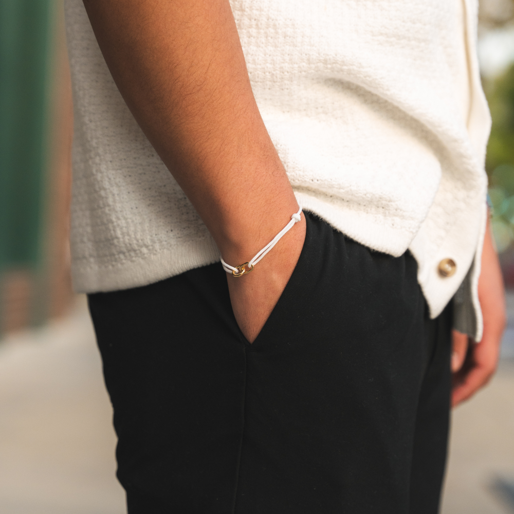 A person wearing a white sweater and black pants, with a gold-colored bracelet on their wrist.