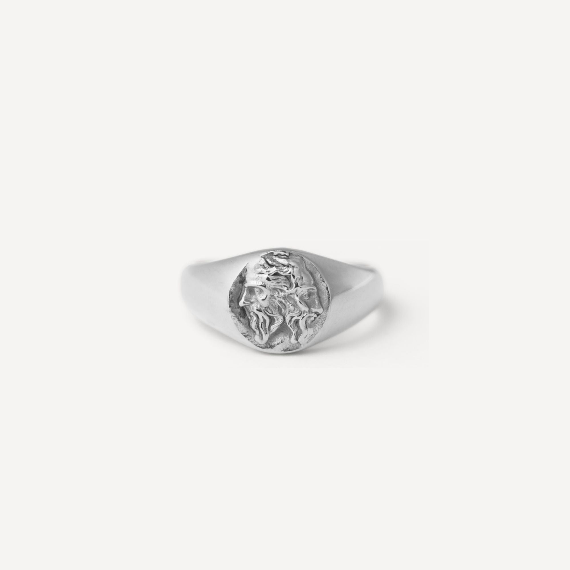 A silver signet ring featuring an embossed lion head design on its oval face, photographed against a clean, light off-white background.
