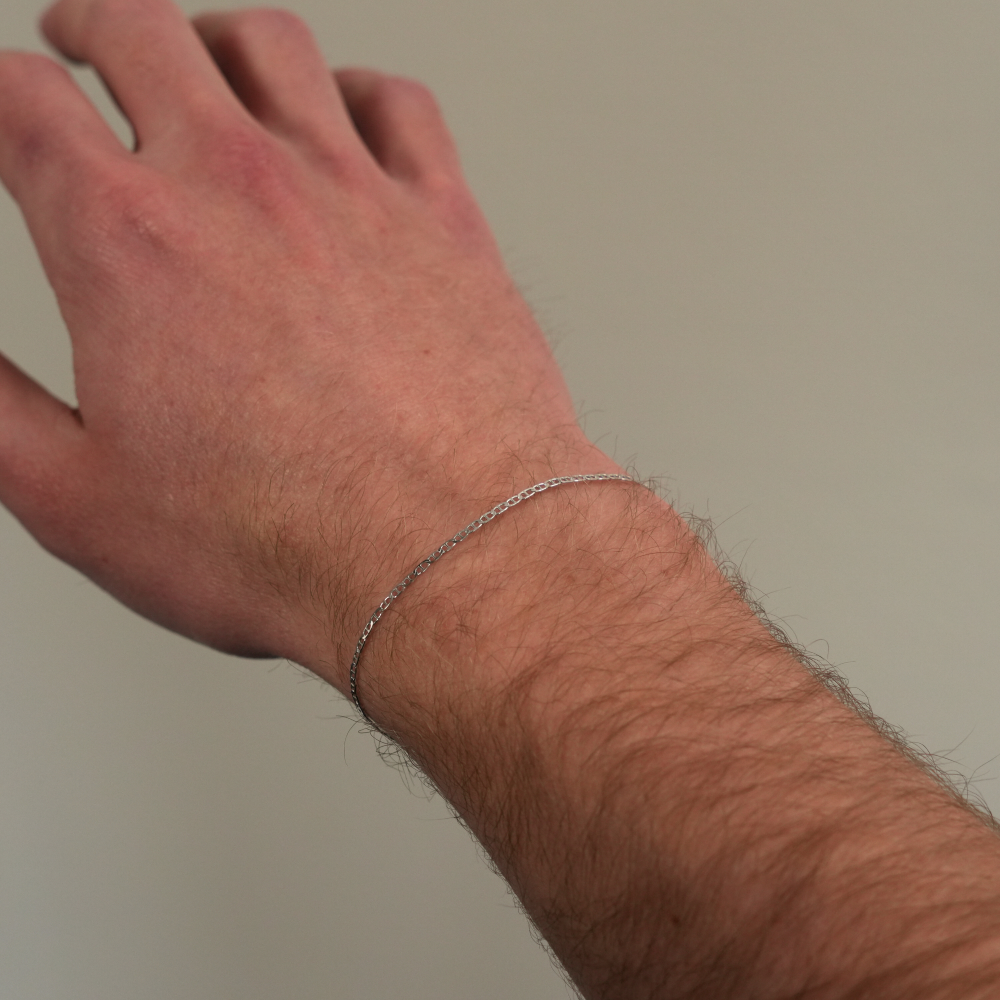 Hand wearing a silver bracelet on a plain background