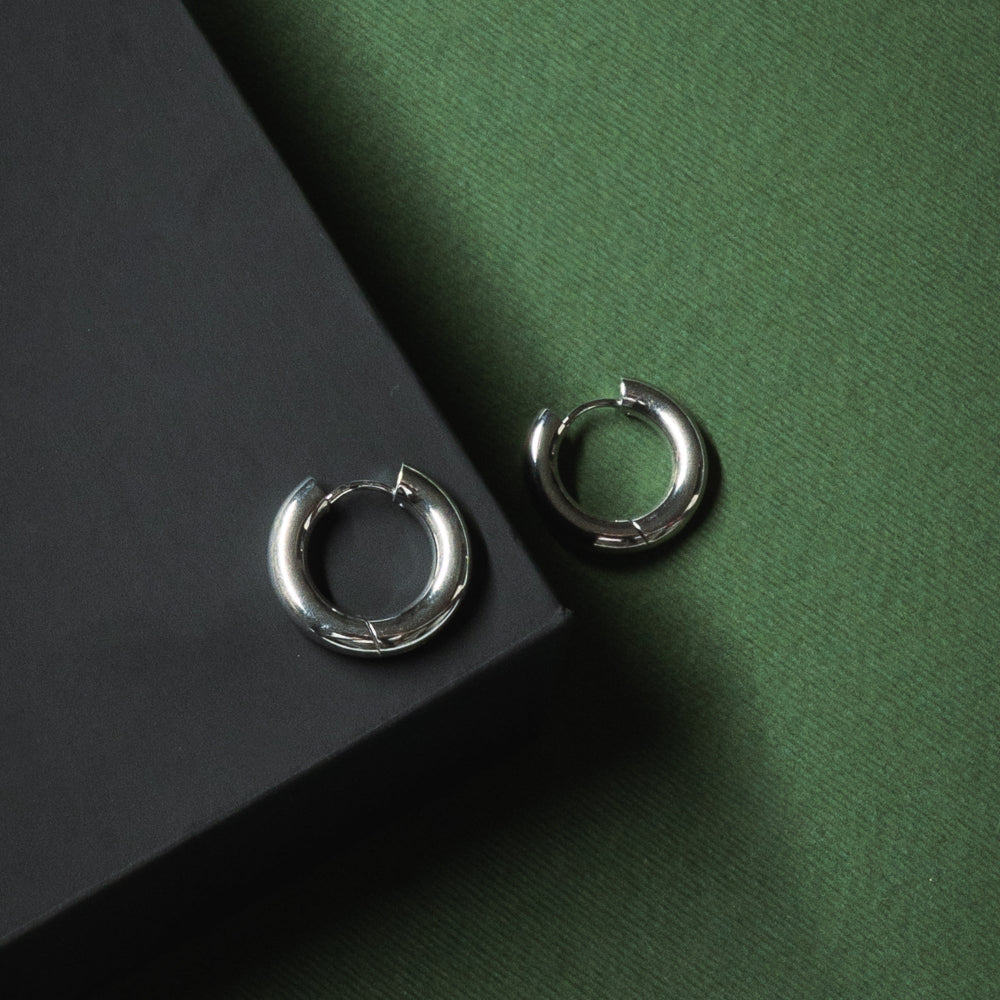 Pair of silver hoop earrings on a dark green surface