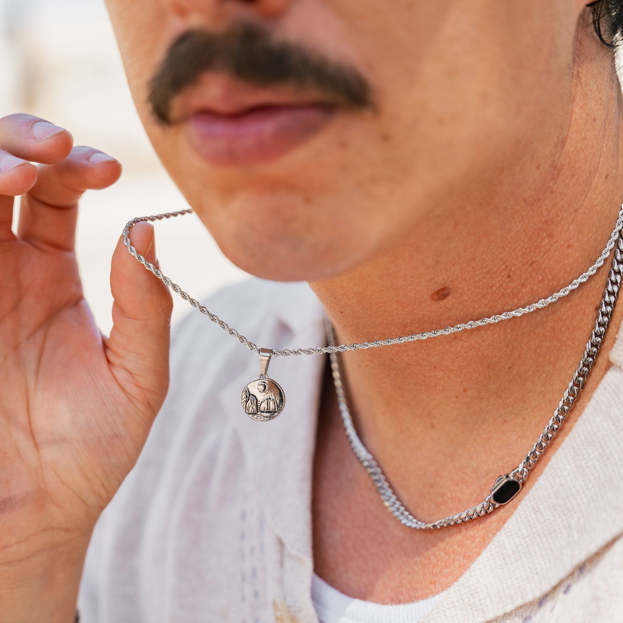 A close-up lifestyle shot of a man wearing a silver chain necklace with a small elephant pendant, holding the chain with his hand.
