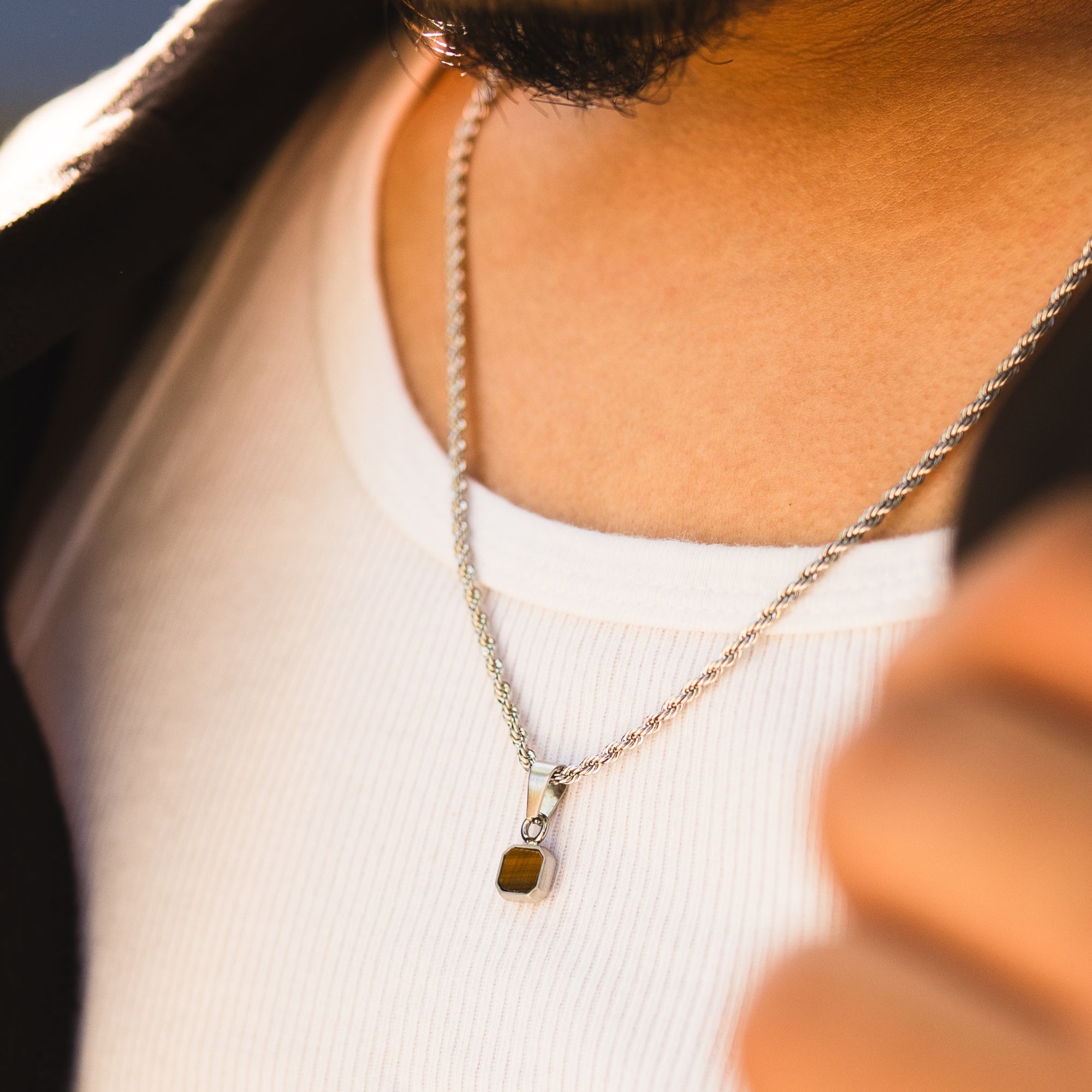 Close-up of a person wearing a silver necklace with a pendant.