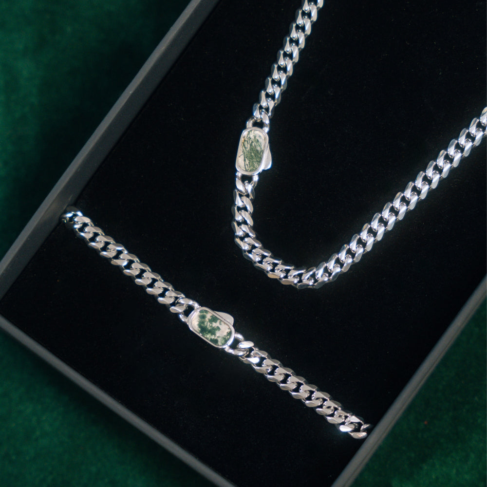 Silver chain bracelet with green gemstones on a black box
