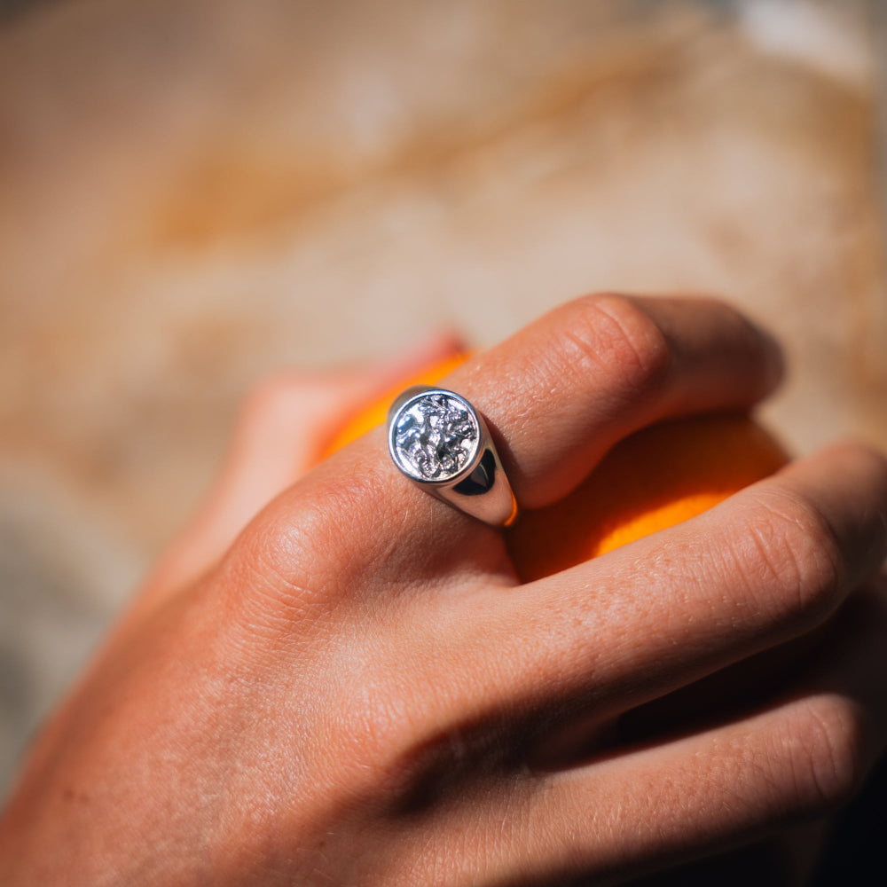 Hand wearing a silver ring with a diamond, holding an orange against a blurred background