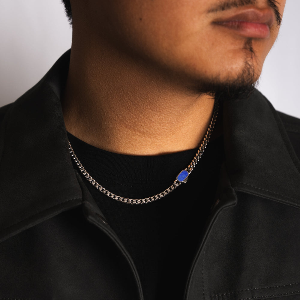 Person wearing a chain necklace with a blue pendant on a plain background