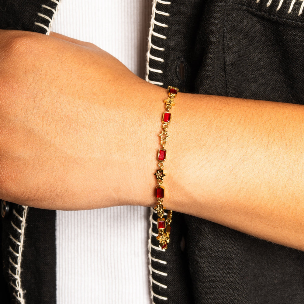 Gold bracelet with red stones on a person's wrist against a neutral background