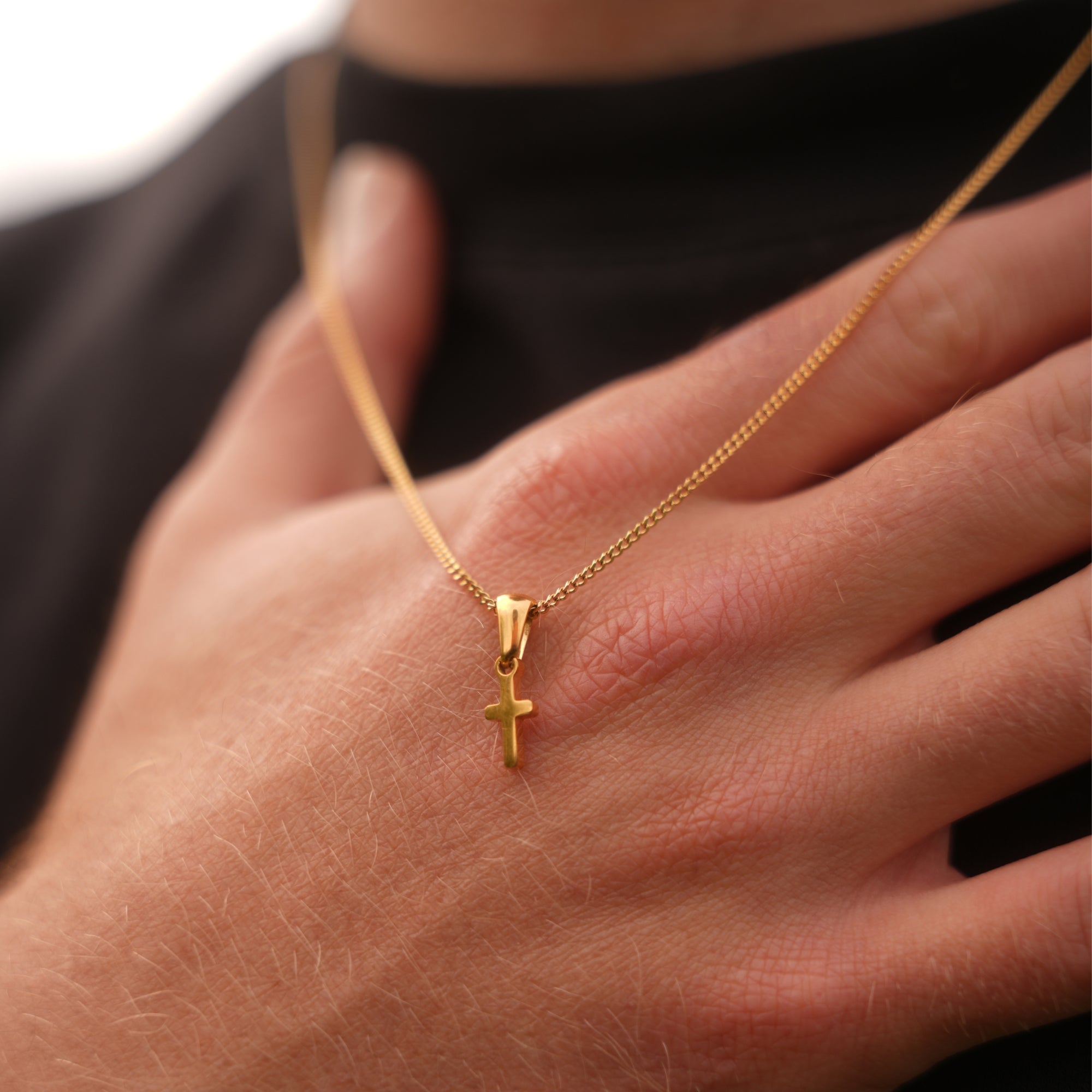 Gold necklace with a cross pendant on a hand against a black background