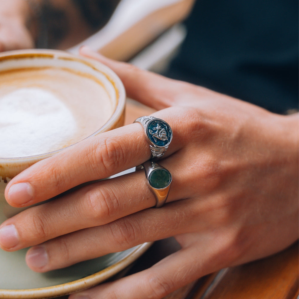 Hand holding a cup of coffee with a decorative ring on a blurred background