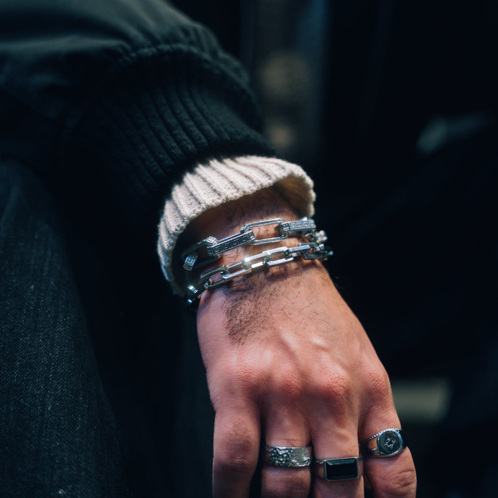 Hand wearing multiple silver bracelets and rings on a dark background