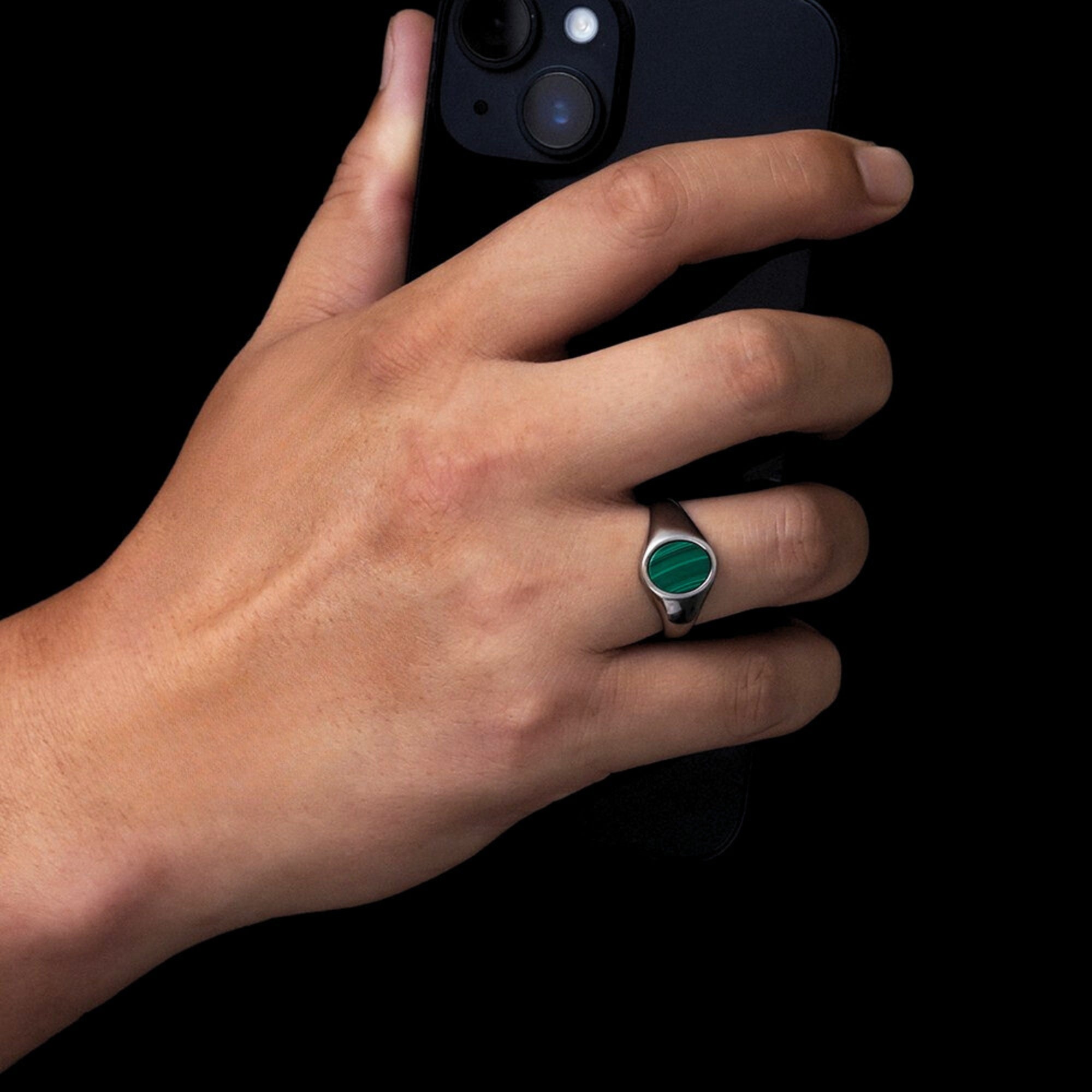 Hand wearing a ring with a green gemstone against a black background