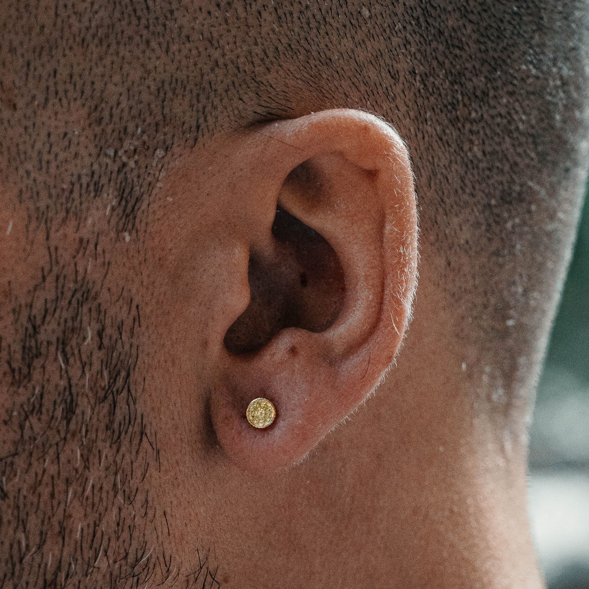 A close-up of a man's ear wearing a small round gold stud earring.