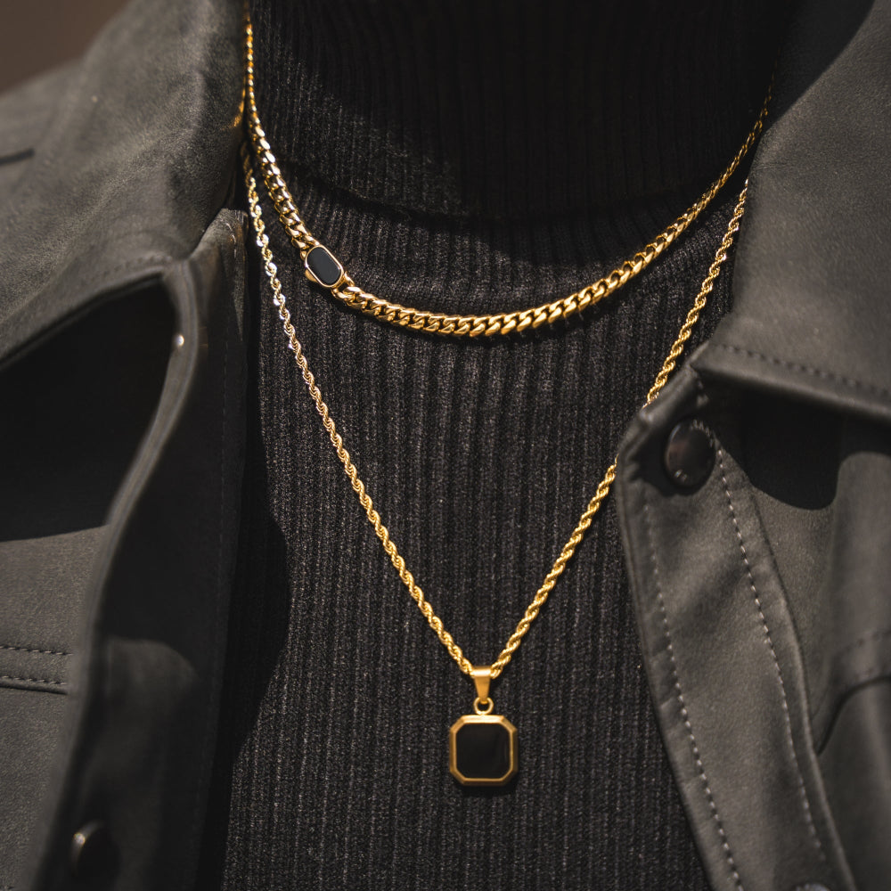 Gold chain necklace with a black pendant on a dark sweater and gray jacket.