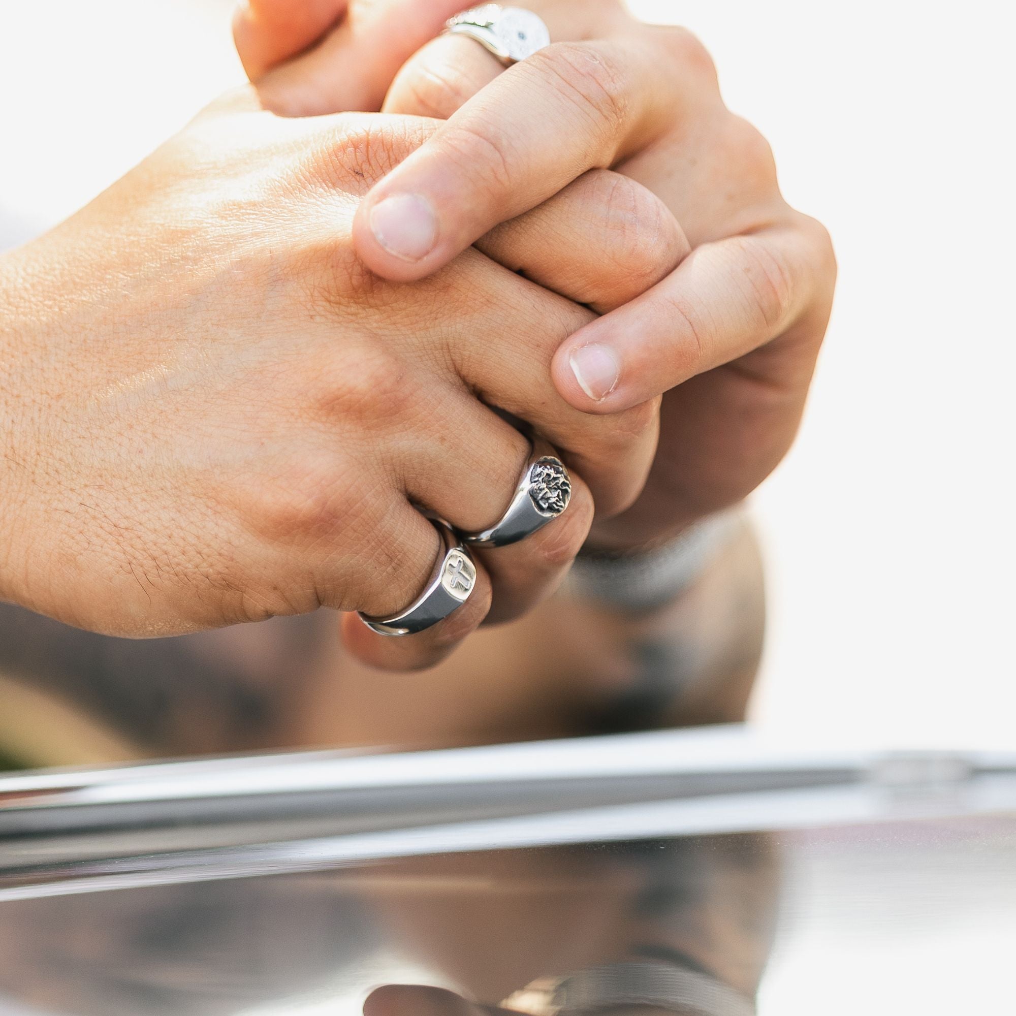 Close-up of two clasped hands wearing silver rings, with one ring featuring a round clear gemstone and the other a textured band design.