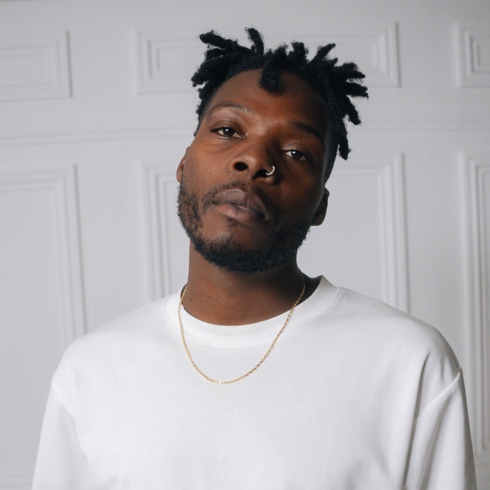 Man wearing a white shirt and gold necklace against a white wall