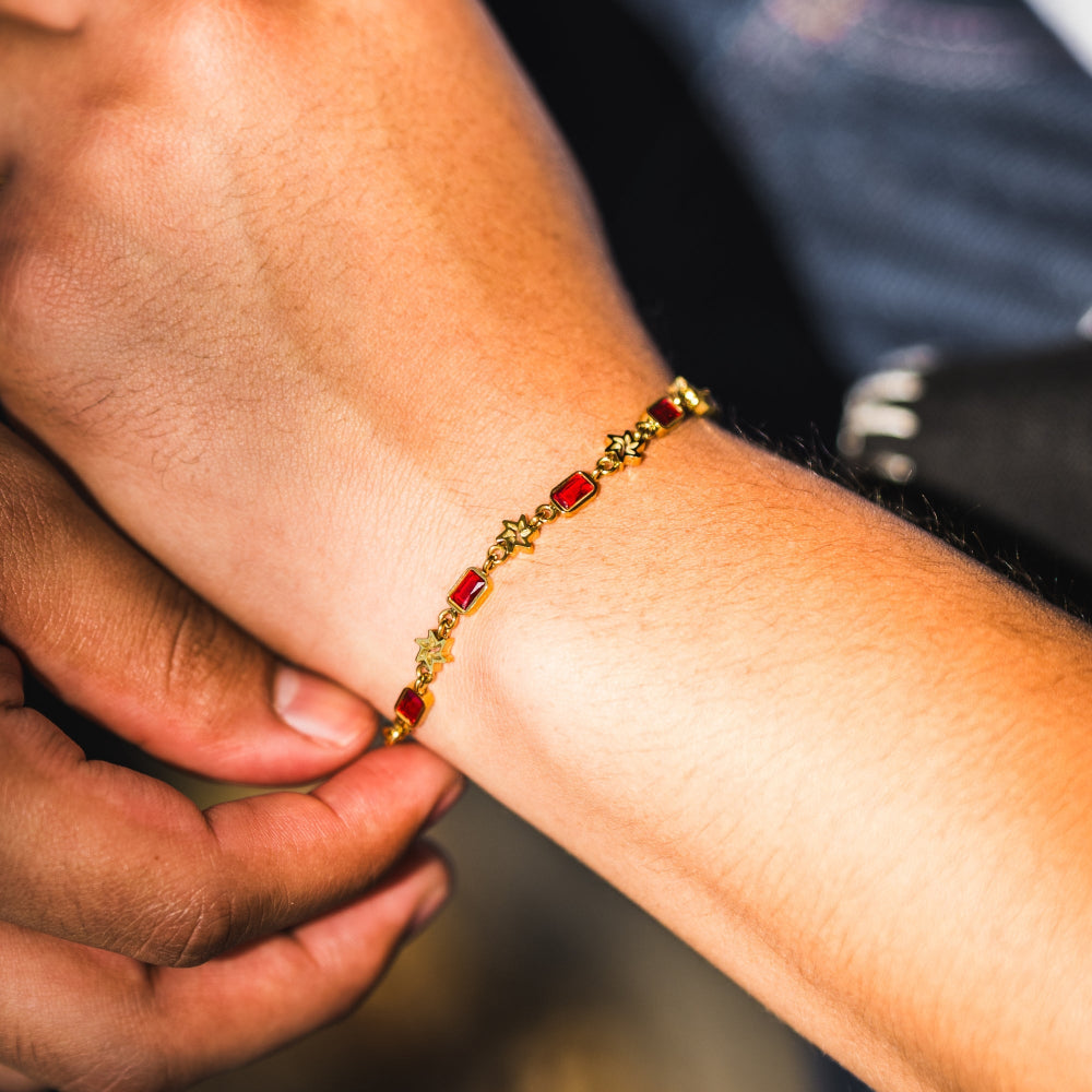 Close-up of a hand adjusting a gold bracelet with red stones on another person's wrist.