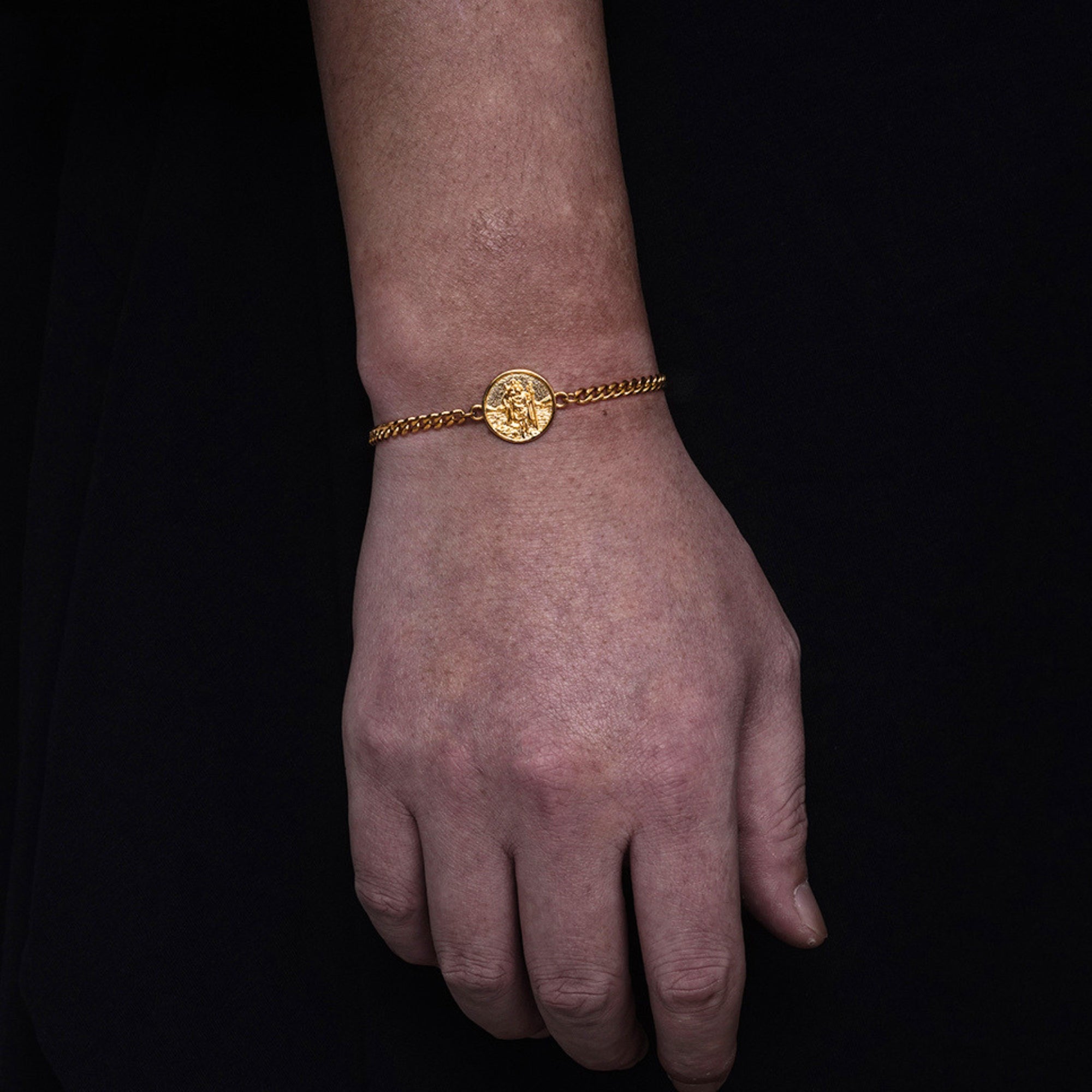 Gold bracelet on a wrist against a black background