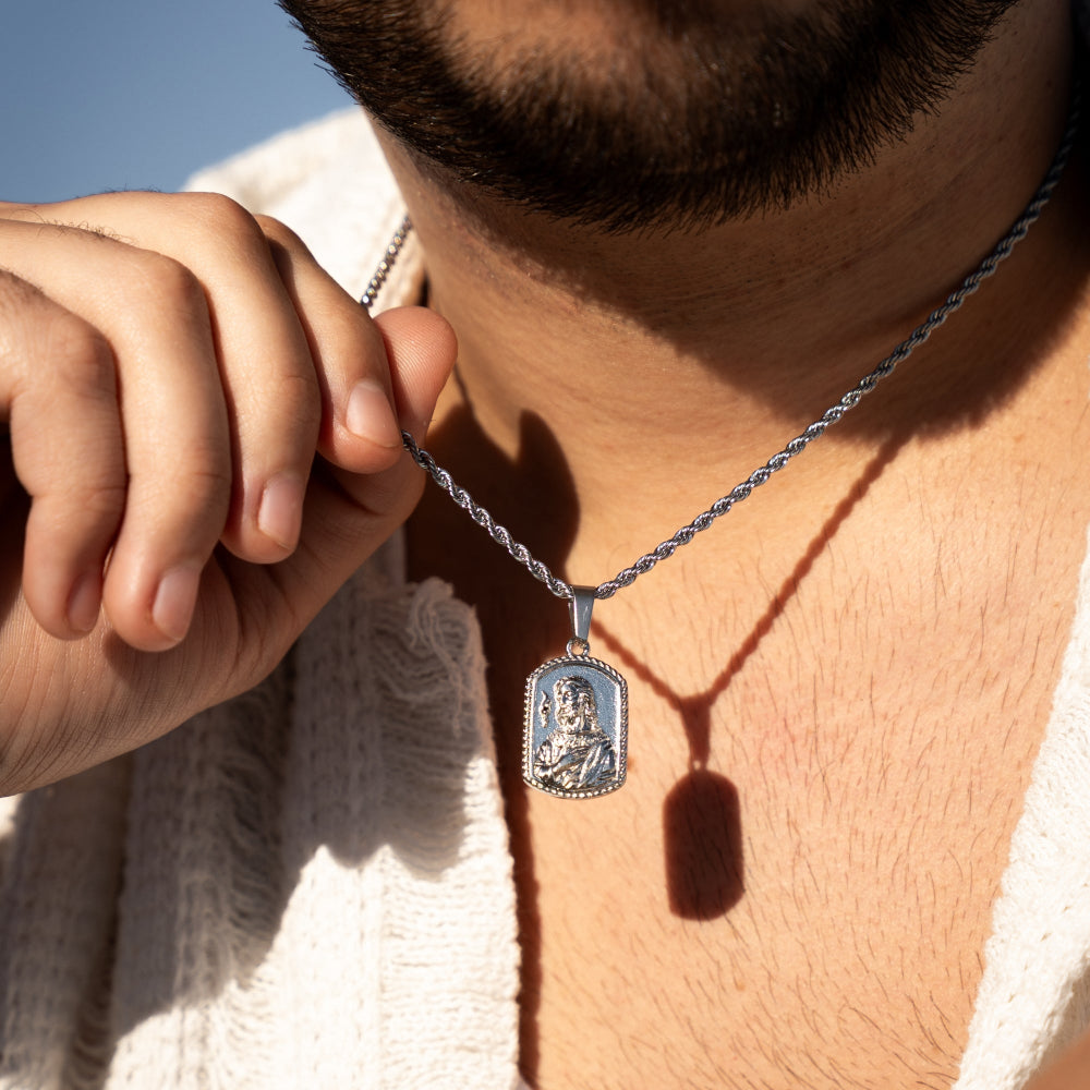 Close-up of a silver pendant necklace being adjusted by a hand against a blurred background