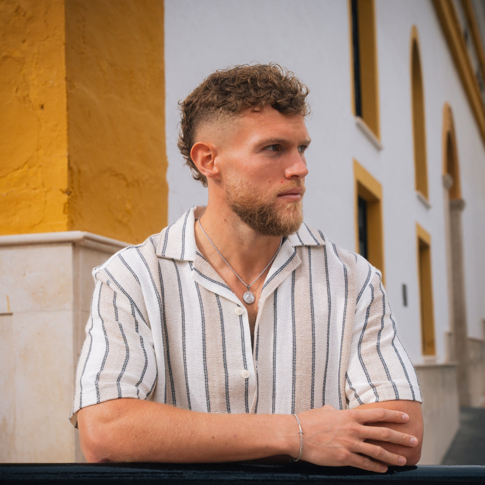 Man with a beard wearing a striped shirt sitting outdoors.