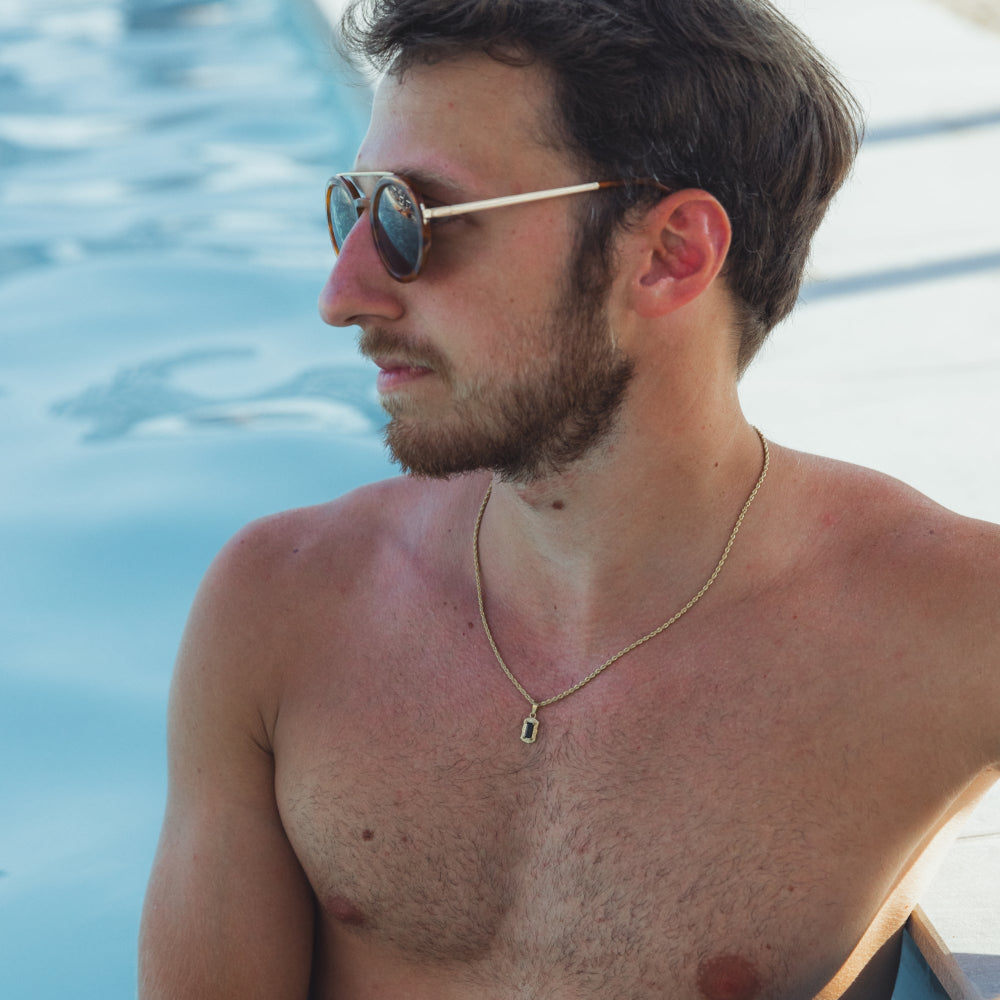 Man wearing sunglasses and a necklace by a pool