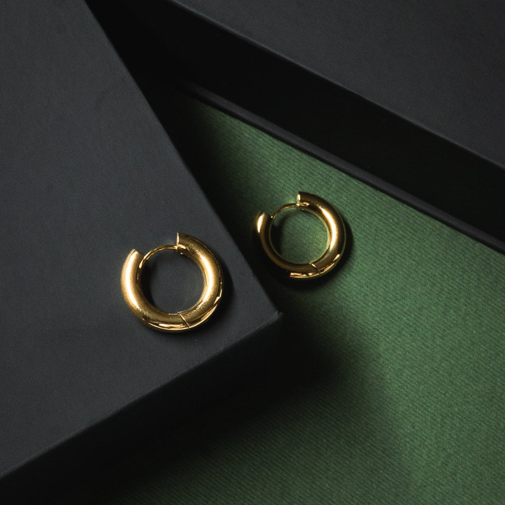 Gold hoop earrings on a dark green surface with a black box.