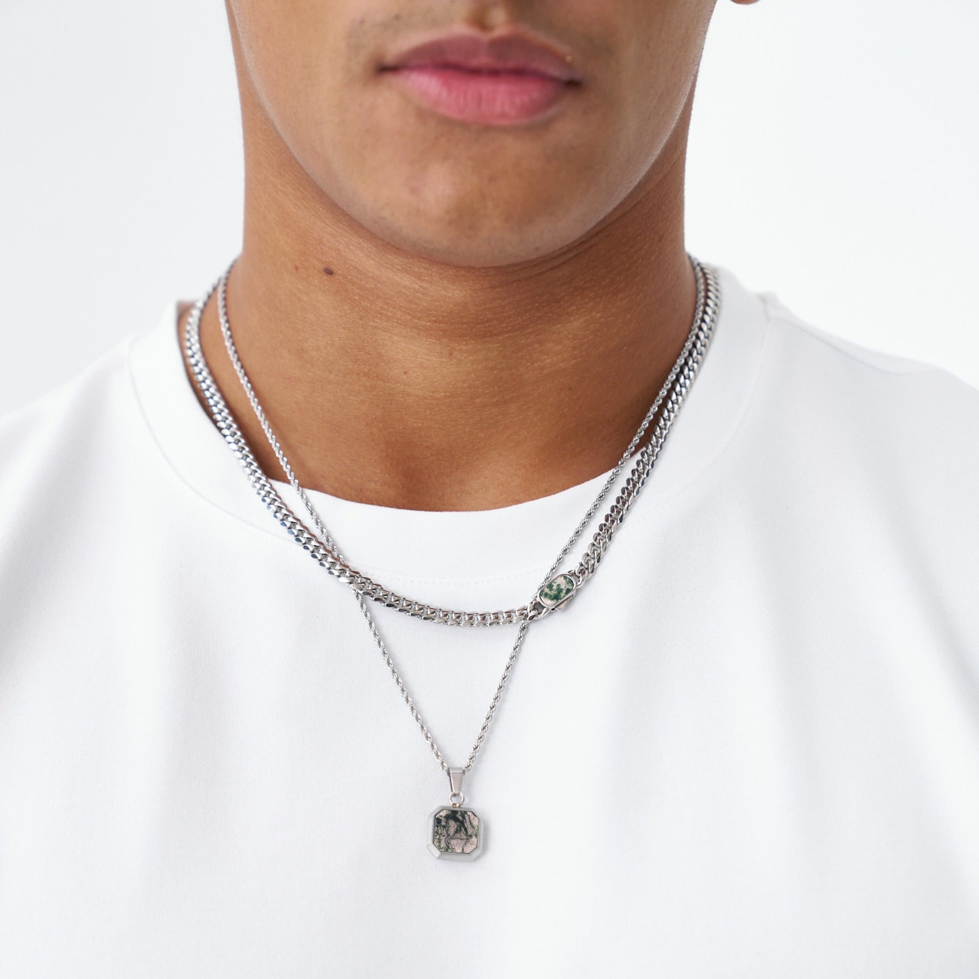 Close-up of a person wearing two silver necklaces on a white background