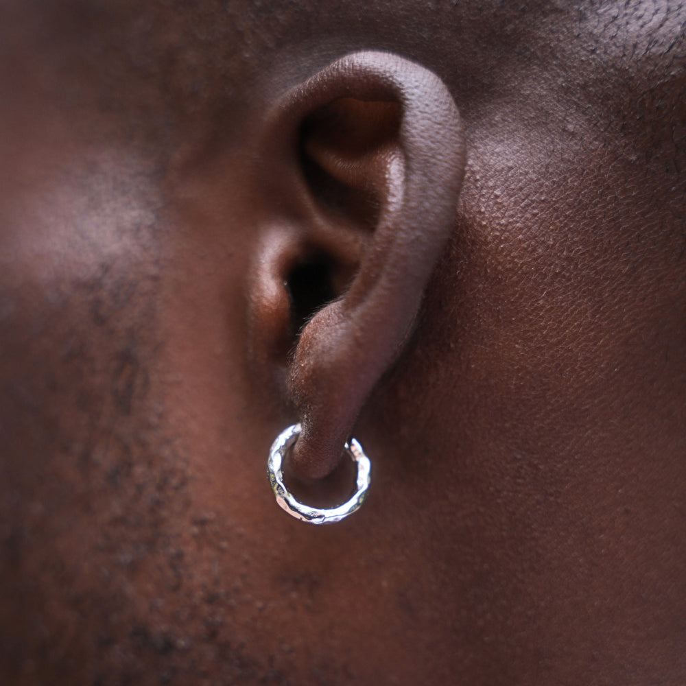 Close-up of an ear wearing a silver hoop earring on a dark skin background
